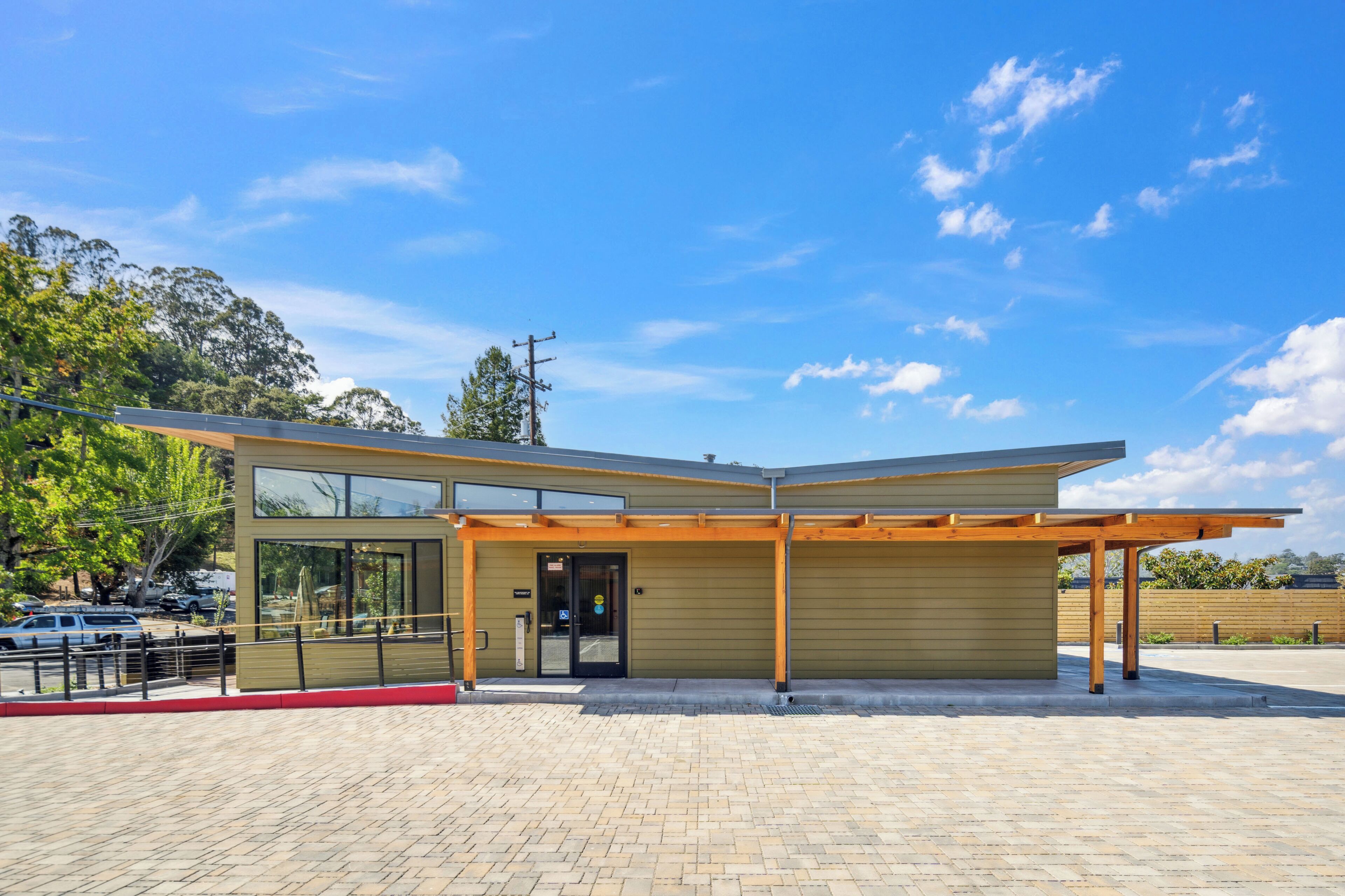 A modern building with a covered entrance, large windows, and a paved area in front.