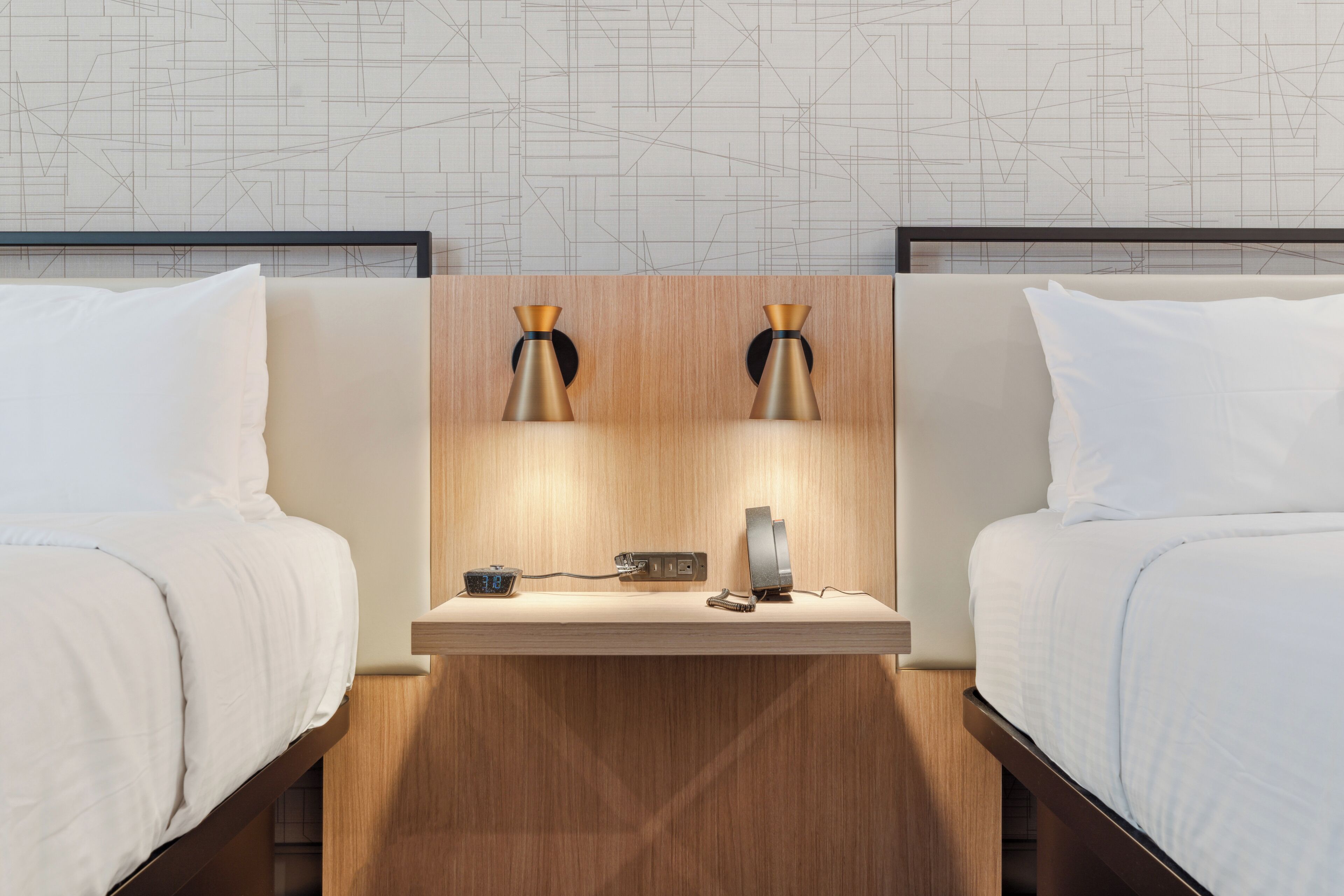 A hotel room with two beds, a wooden nightstand, a digital clock, and a small table lamp.