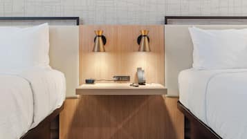 Habitación de hotel con dos camas, una mesita de noche de madera, un reloj digital y una lámpara de mesa pequeña.