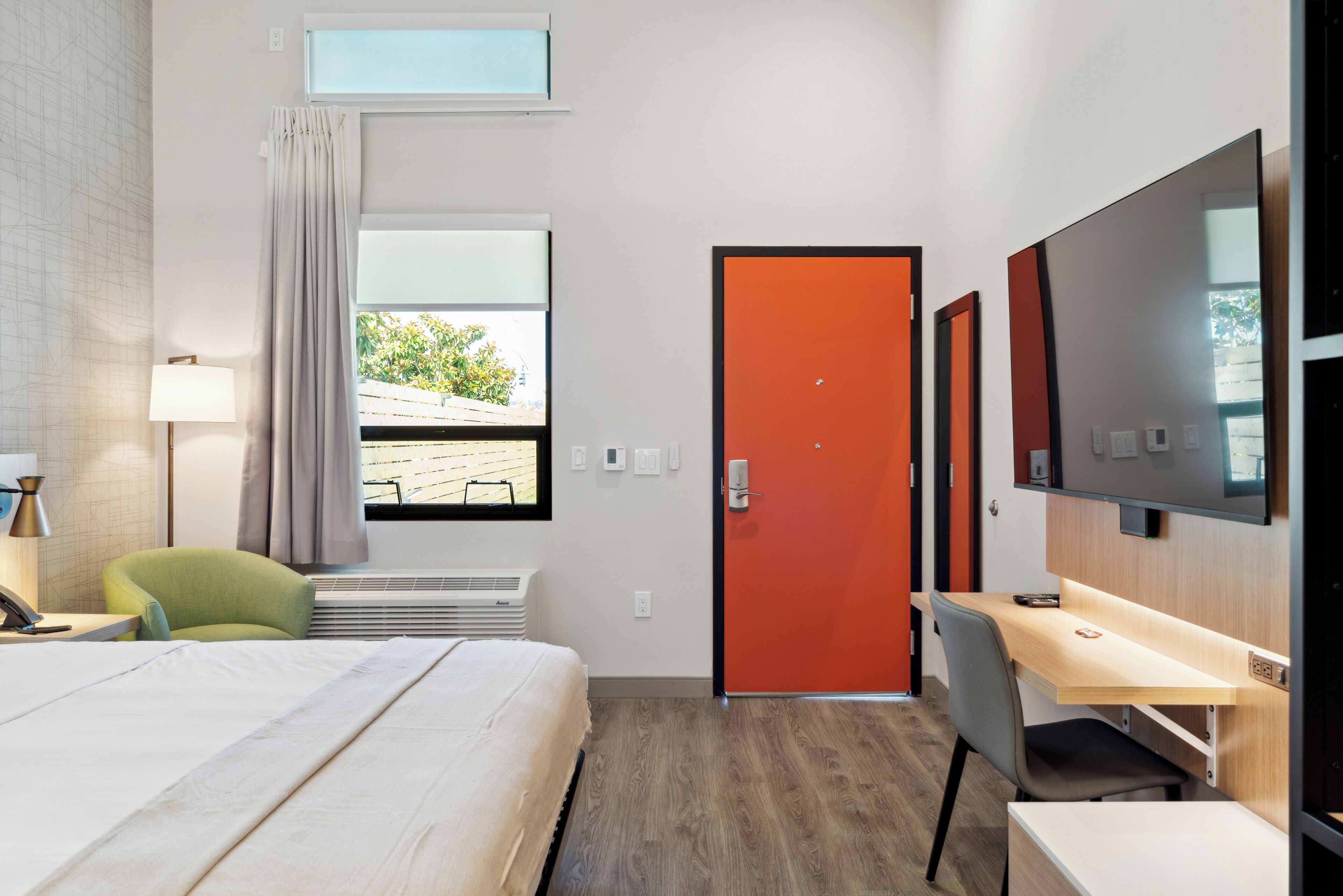 A hotel room with a bed, a desk, a chair, a TV, and a window with curtains.