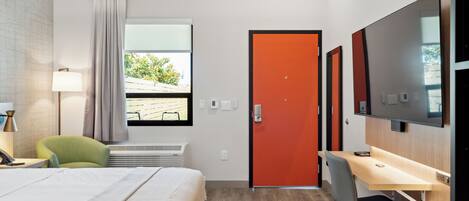A hotel room with a bed, a desk, a chair, a TV, and a window with curtains.