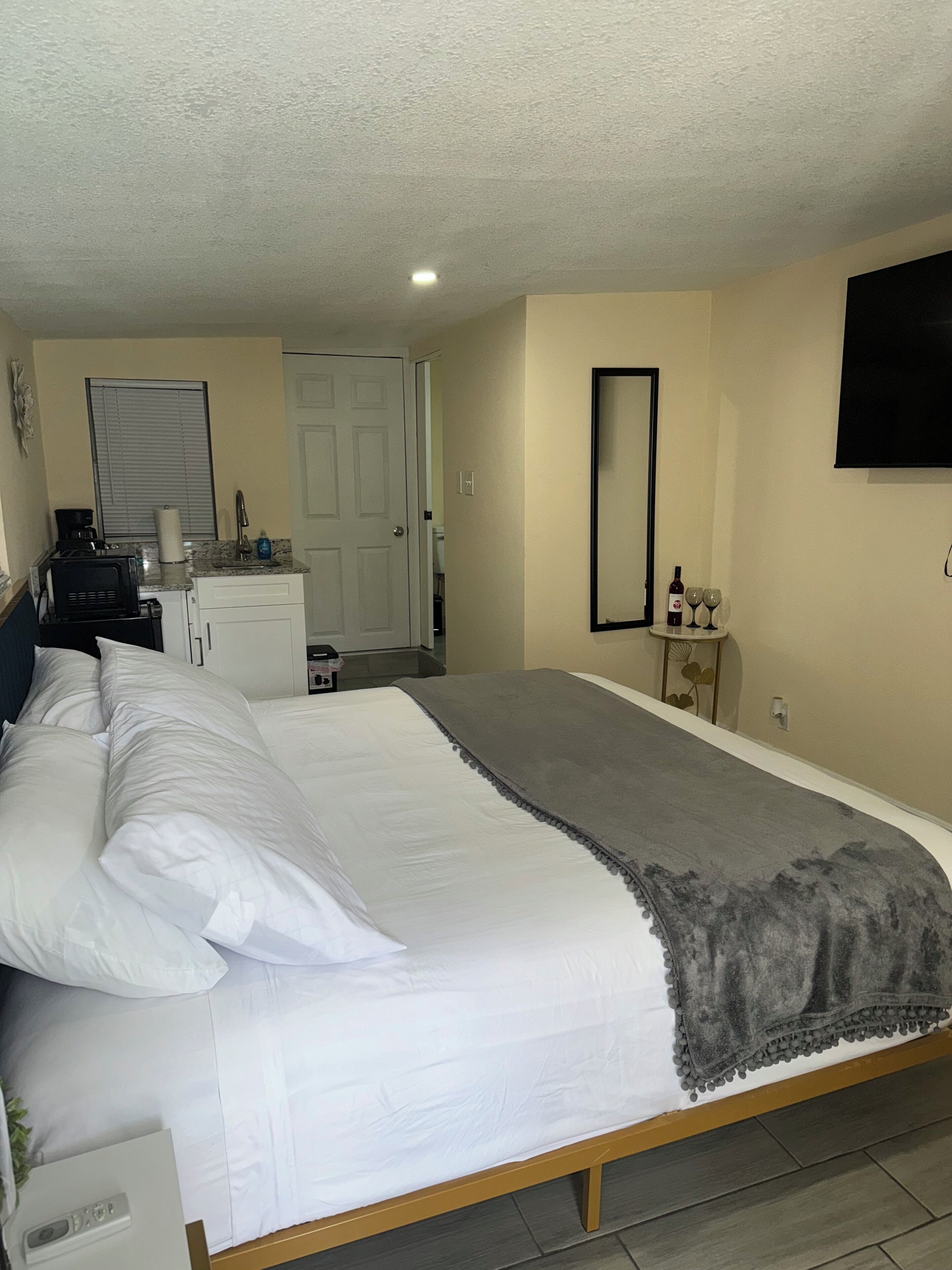 A bedroom with a bed, a dresser, a mirror, and a TV on the wall.