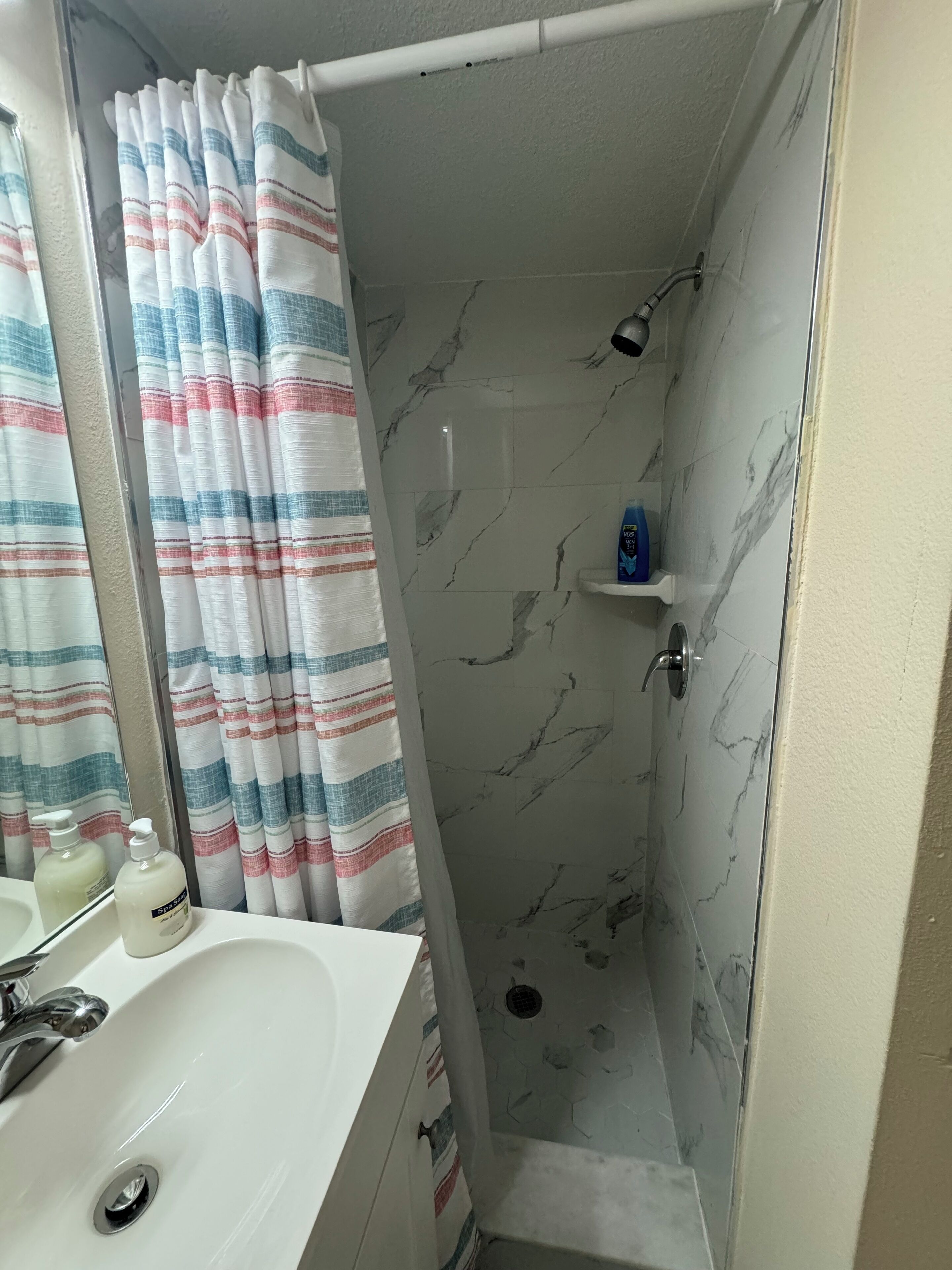A bathroom with a shower, a sink, and a mirror.