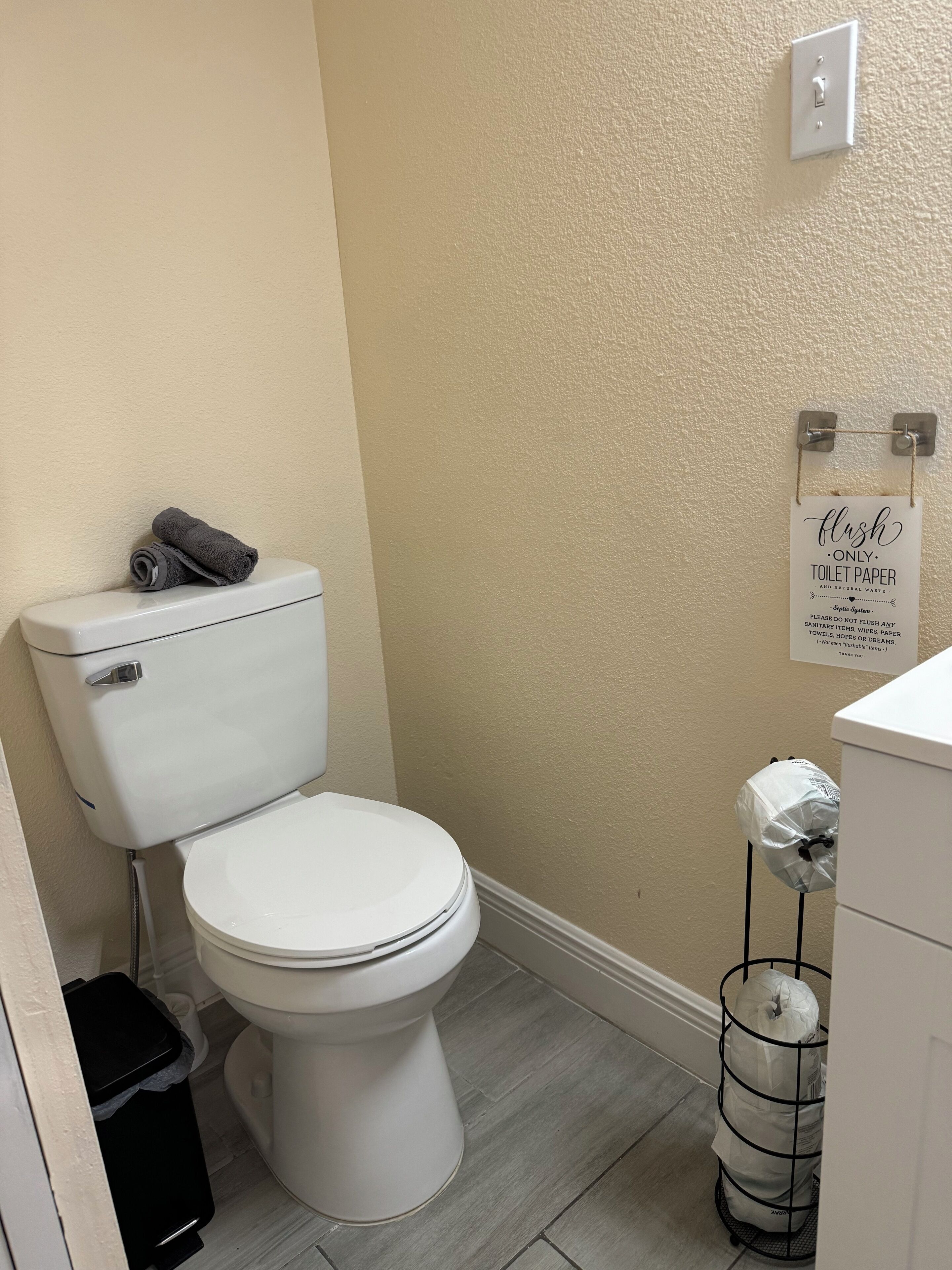 A toilet with a white tank and lid, a roll of toilet paper on a holder, and a sign above the toilet instructing to flush only toilet paper.