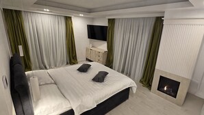 Un dormitorio moderno con cama, televisión, chimenea y cortinas.