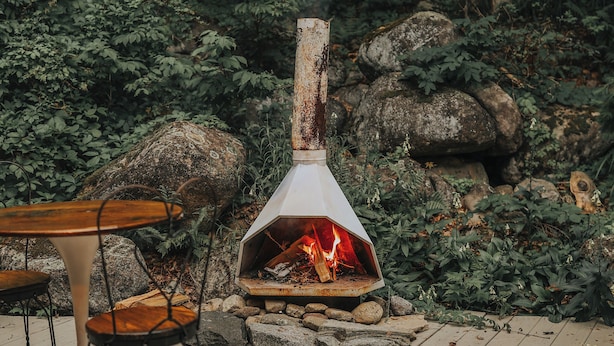 A rustic outdoor seating area with a wood-burning stove, surrounded by rocks and greenery. - Historic farmhouse by the river in Keene, NY near Lake Placid & Whiteface Mt. (Keene)