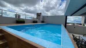 Une piscine sur le toit, offrant une vue sur les bâtiments environnants et un ciel nuageux.