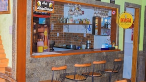 A bar area with a brick wall, bar stools, shelves with bottles, and a sign for 'Devassa'.