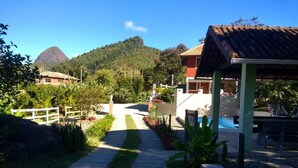 A pathway leading to a building with a red roof, surrounded by greenery and a mountain in the background.