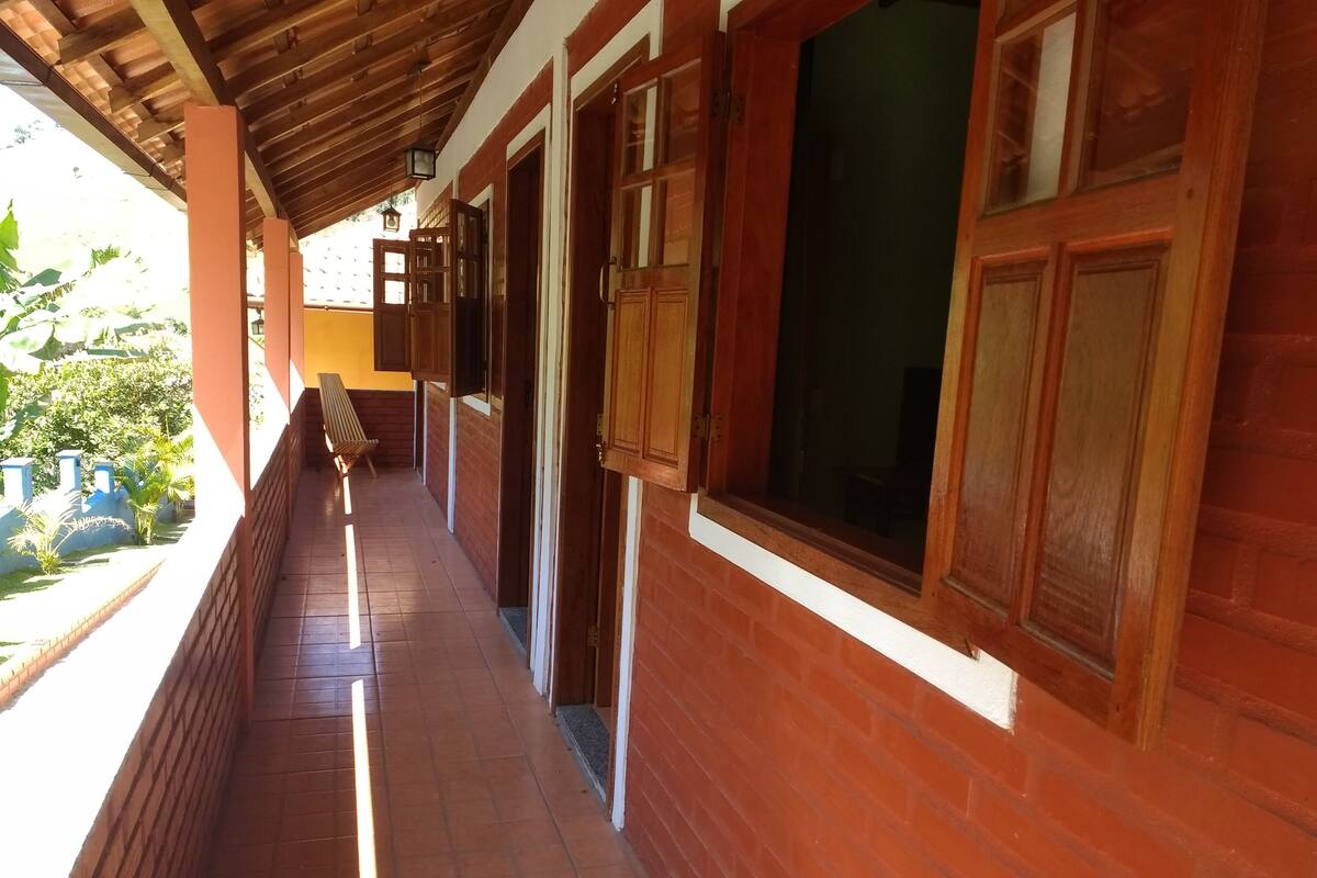 A covered corridor with wooden doors and windows, a bench, and a tiled floor.