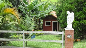 A small brick building with a red roof, surrounded by lush greenery and a wooden fence.