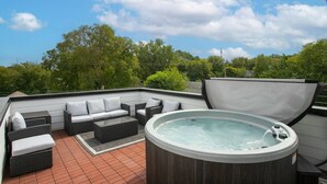 Una terraza en la azotea con jacuzzi, zona de estar exterior y vistas a árboles y cielo.