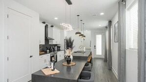 Una cocina moderna con una isla central, iluminación colgante y un comedor con sillas.