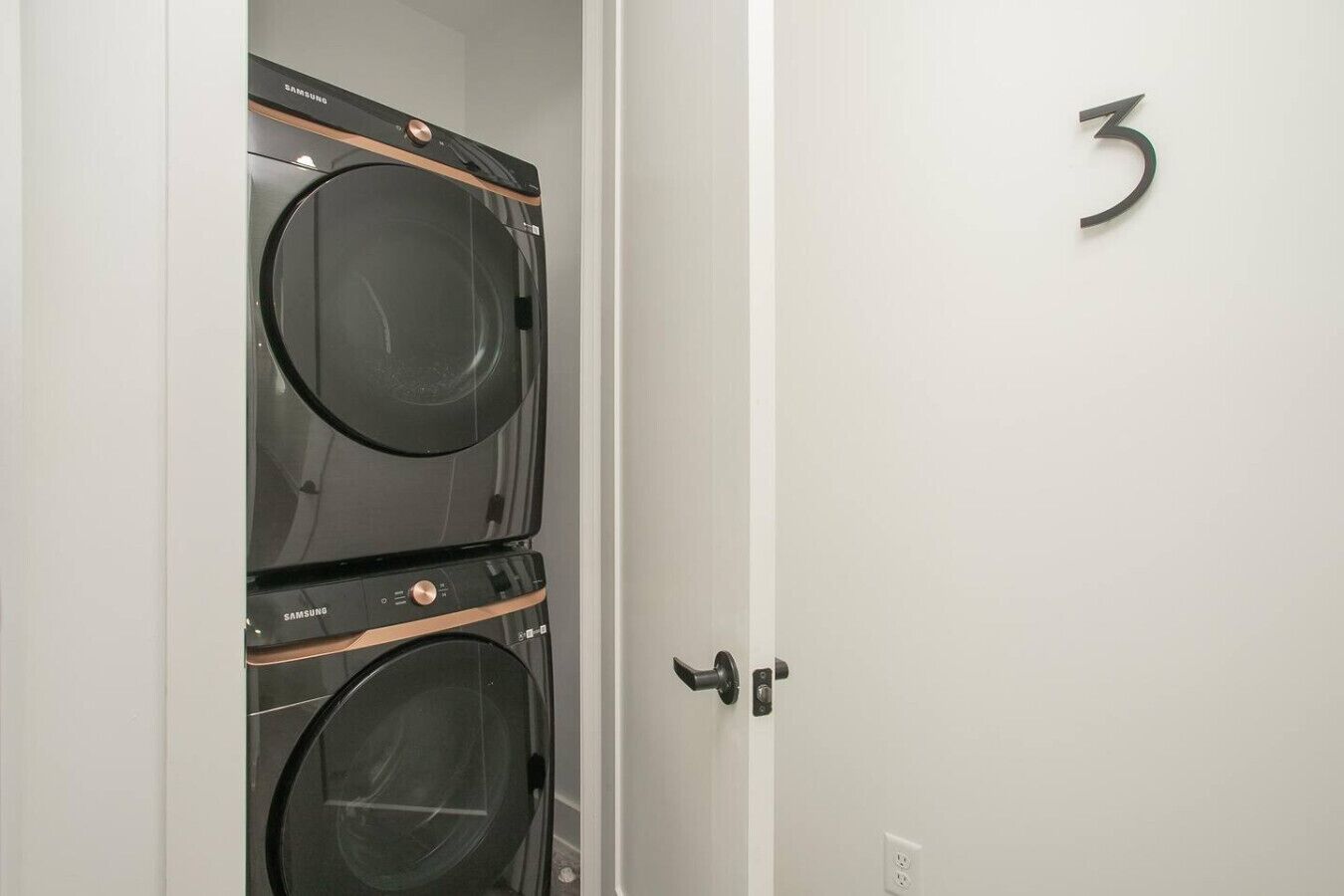 A laundry room with two Samsung washing machines and a door with the number 3 on it.