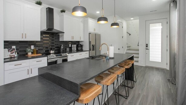 Una cocina moderna con armarios blancos, una isla central con taburetes de bar, estufa e iluminación colgante.