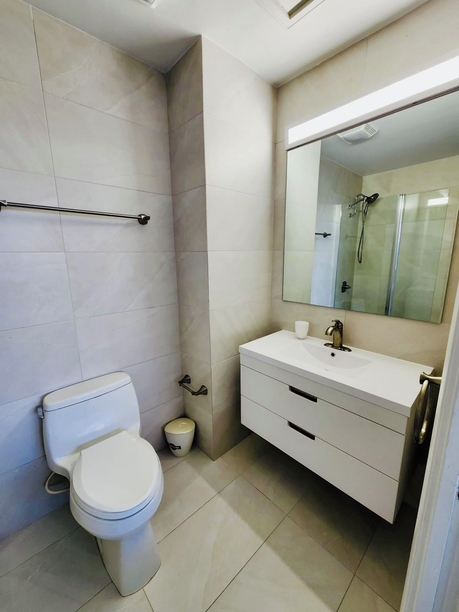 A modern bathroom with a toilet, a sink, a mirror, and a shower.