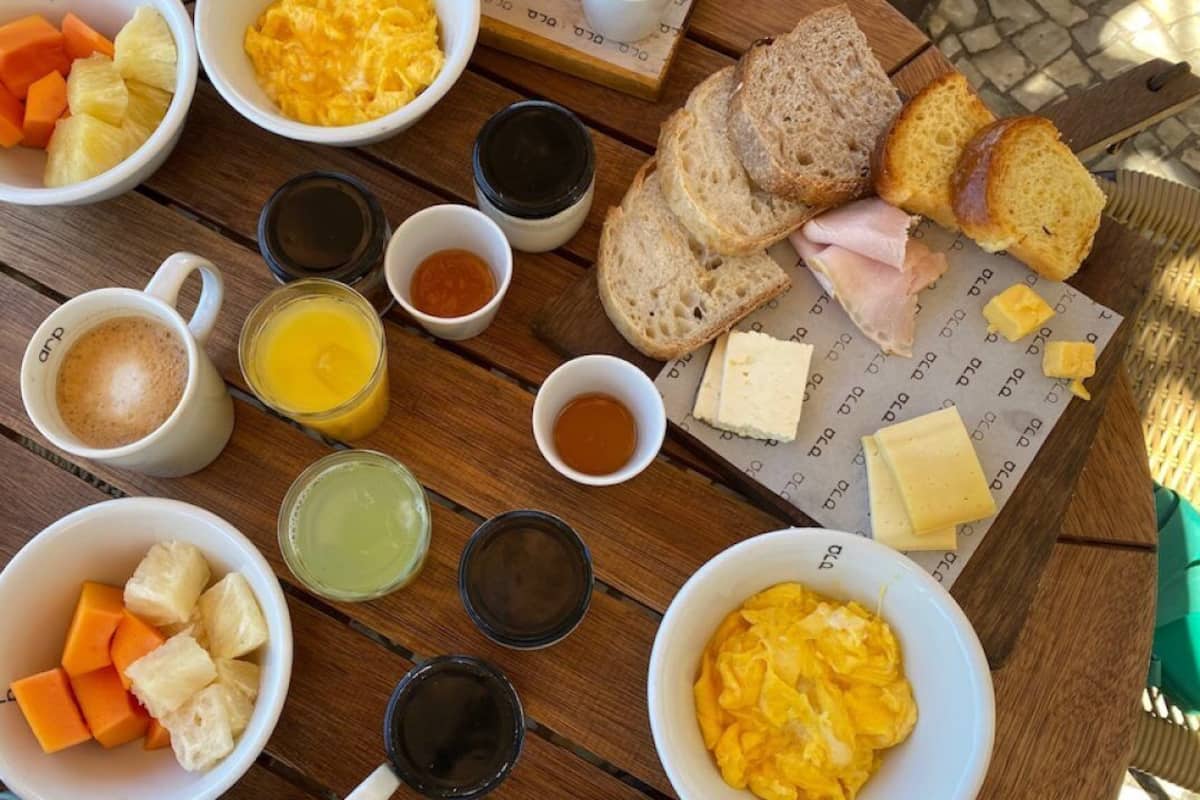 Uma mesa de café da manhã com diversos alimentos, como ovos, pão, queijo e frutas.
