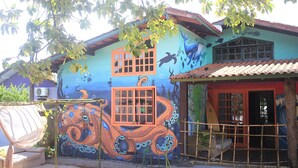 A house with a mural of an octopus on the side, a window with a grid pattern, and a door with a red frame. - Off Ocean Hostel (Florianópolis)