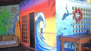 A room with a colorful mural, a wooden table, and a map on the wall. - Off Ocean Hostel (Florianópolis)