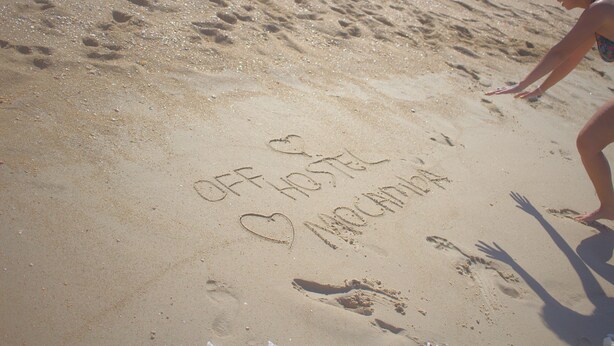 A sandy beach with footprints and the words "OFF HOSTEL" and "MANCHESTER" written on the sand. - Off Ocean Hostel (Florianópolis)