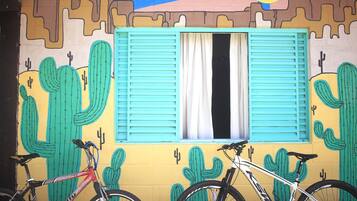 A mural with cacti and a window with blue shutters.