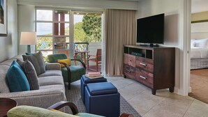 A hotel room with a sofa, ottoman, TV, and a view of the outdoors.