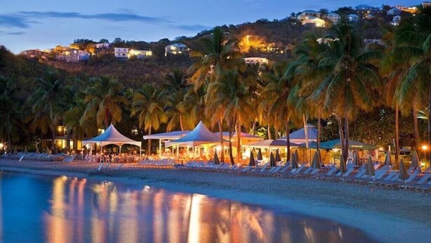 A beachfront hotel with palm trees, beach umbrellas, and a pool.