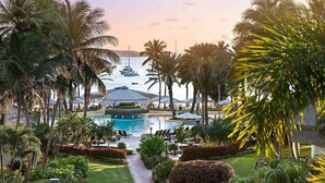 A resort with a swimming pool, palm trees, and boats in the background.