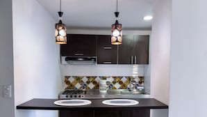 A modern kitchen with dark cabinets, a gas stove, two white bar stools, and decorative hanging lights. - SPACIOUS AND LUXURIOUS APARTASUITE IN THE CENTER OF THE CITY (Cartago)