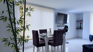 A modern dining area with a table and chairs, a large potted plant, a flat-screen TV mounted on the wall, and a sofa in the background. - SPACIOUS AND LUXURIOUS APARTASUITE IN THE CENTER OF THE CITY (Cartago)