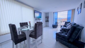 A modern living room with a glass dining table, dark grey chairs, a grey sofa, and a TV mounted on the wall. - SPACIOUS AND LUXURIOUS APARTASUITE IN THE CENTER OF THE CITY (Cartago)