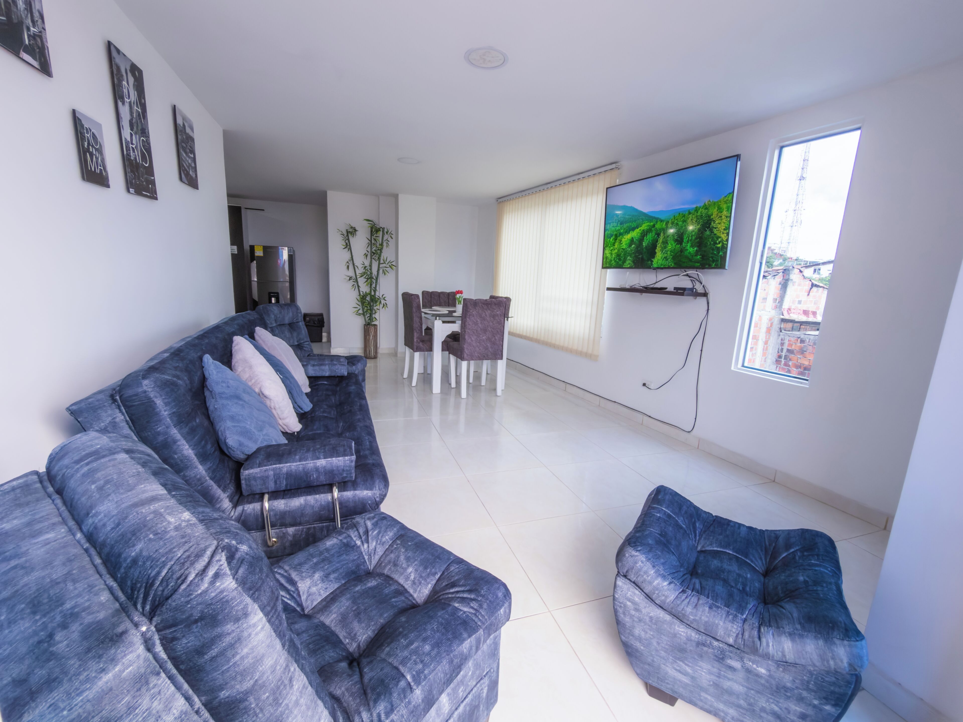 A modern living room with a blue sofa, a dining area, and a TV mounted on the wall.