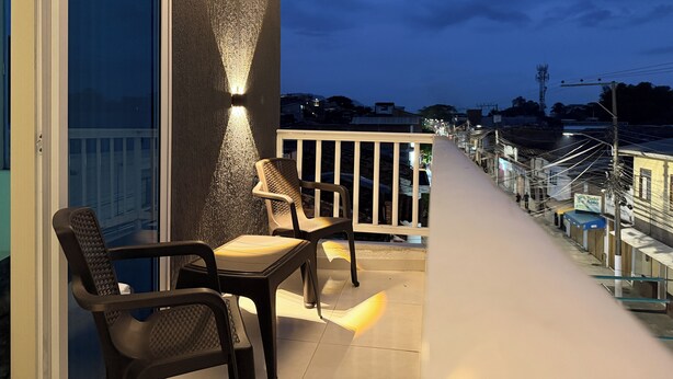 A balcony with two chairs, a railing, and a view of a street at dusk. - SPACIOUS AND LUXURIOUS APARTASUITE IN THE CENTER OF THE CITY (Cartago)