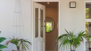 Een houten veranda met aan weerszijden twee grote zwarte plantenbakken, een witte deur en een klein rond raam erboven.