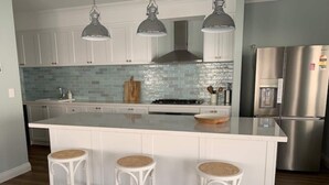 Una cocina moderna con armarios blancos, una isla grande con taburetes, electrodomésticos de acero inoxidable y un backsplash de azulejos azules.