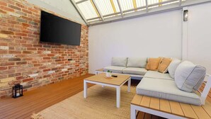 Een gezellige woonkamer met een bakstenen muur, een flatscreen televisie, een bank en een houten salontafel.