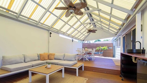 Een moderne, open woonkamer met een houten vloer, een modulaire bank, een eettafel met stoelen en een keuken met een spoelbak en aanrecht.