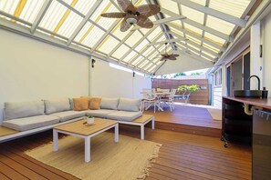 A modern, open-plan living area with a wooden floor, a sectional sofa, a dining table with chairs, and a kitchen area with a sink and countertop. - Manning private escape | Swan BnB Management (Manning)
