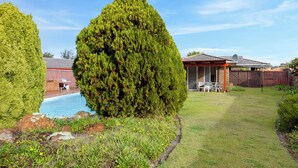 Un jardin avec une piscine, un patio couvert et une zone délimitée par une clôture.