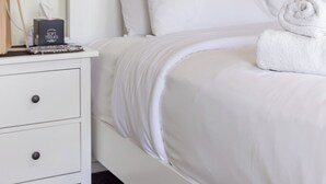 Une chambre à coucher avec un lit blanc, une table de chevet avec une lampe et un tableau représentant une vache accroché au mur.