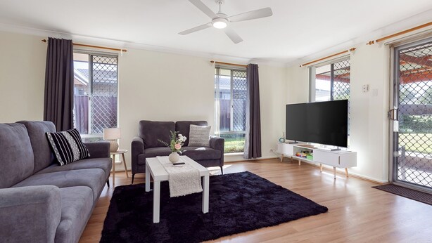 Un salon moderne avec un canapé gris, une table basse blanche, un tapis noir, un fauteuil gris et un téléviseur à écran plat.