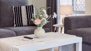 Un salon moderne avec une table basse blanche, un vase de fleurs, un canapé gris et un rideau gris.