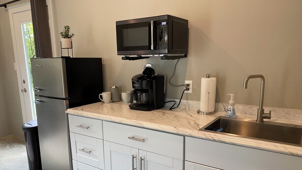A compact kitchen with a refrigerator, microwave, coffee maker, and sink. - Modern 1-bedroom cottage in historic downtown Mount Vernon. (Mount Vernon)