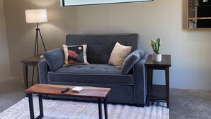 A modern living room with a grey sofa, a wooden coffee table, a floor lamp, and a small plant. - Modern 1-bedroom cottage in historic downtown Mount Vernon. (Mount Vernon)