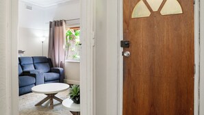 Una habitación con puerta de madera, un sofá azul, una mesa blanca y una planta.