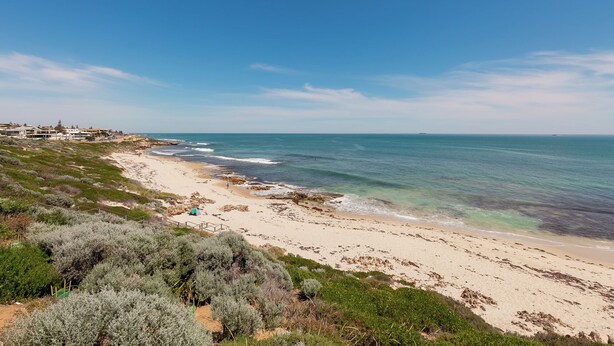 Un paisaje costero con una playa arenosa, afloramientos rocosos y un cielo azul despejado.