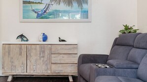 Un salón con un sofá gris, un mueble de madera con objetos decorativos y un cuadro con una escena de playa.