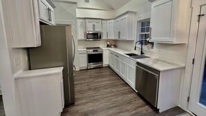 Una cocina con armarios blancos, electrodomésticos de acero inoxidable y suelo de madera.