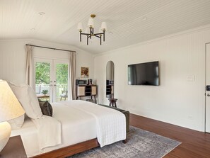 A bedroom with a bed, a television, a desk with a chair, and a window with curtains.