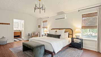Une chambre à coucher avec un grand lit, des lampes de chevet, un lustre, une fenêtre avec des stores et un plancher en bois.